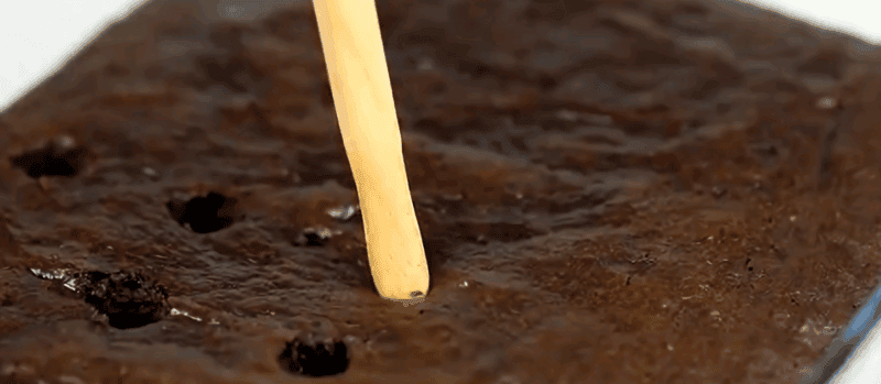 Poking holes in a chocolate cake.