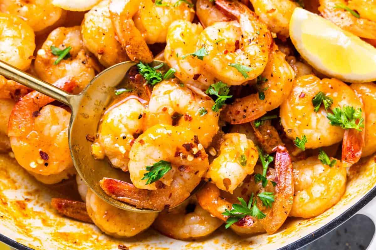 partial close-up view of garlic butter shrimp in a white pan with a spoon.