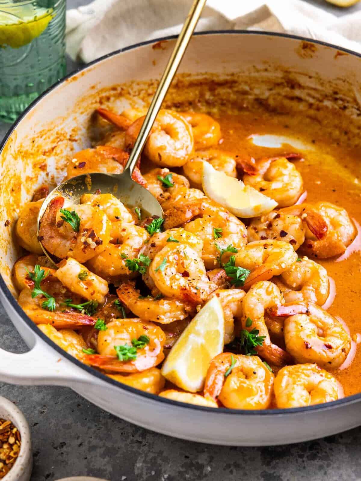 three-quarters view of garlic butter shrimp in a white pan with a spoon and lemon wedges.