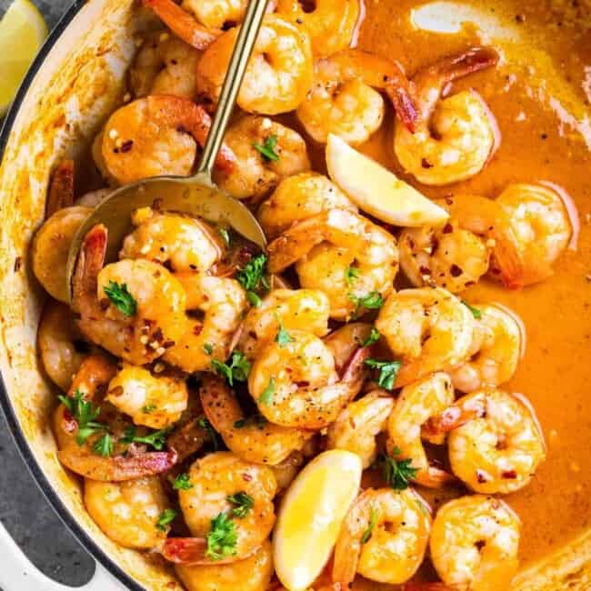 overhead view of garlic butter shrimp in a white pan with a spoon and lemon wedges.