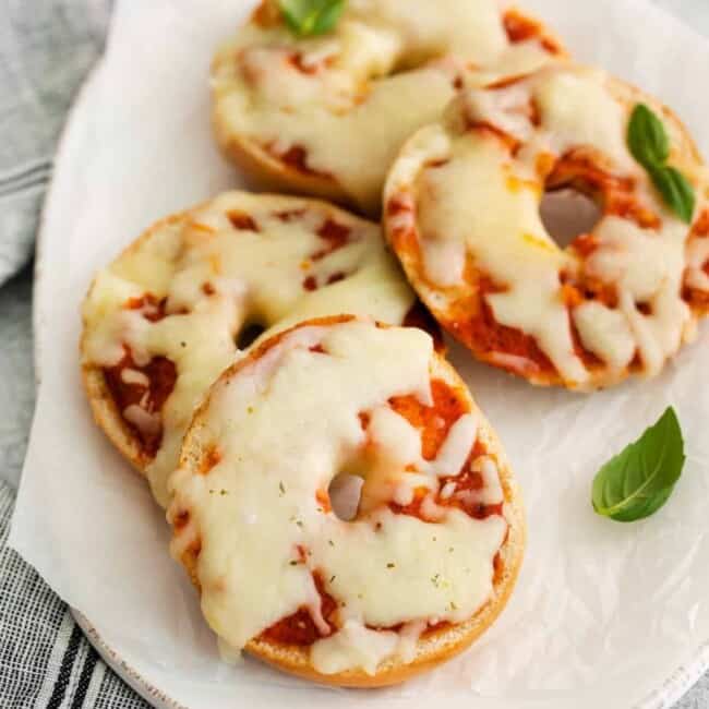 three-quarters view of 4 pizza bagels on an oval serving dish.