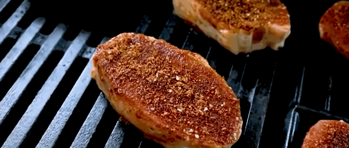 Pork chops with seasoning on a grill.