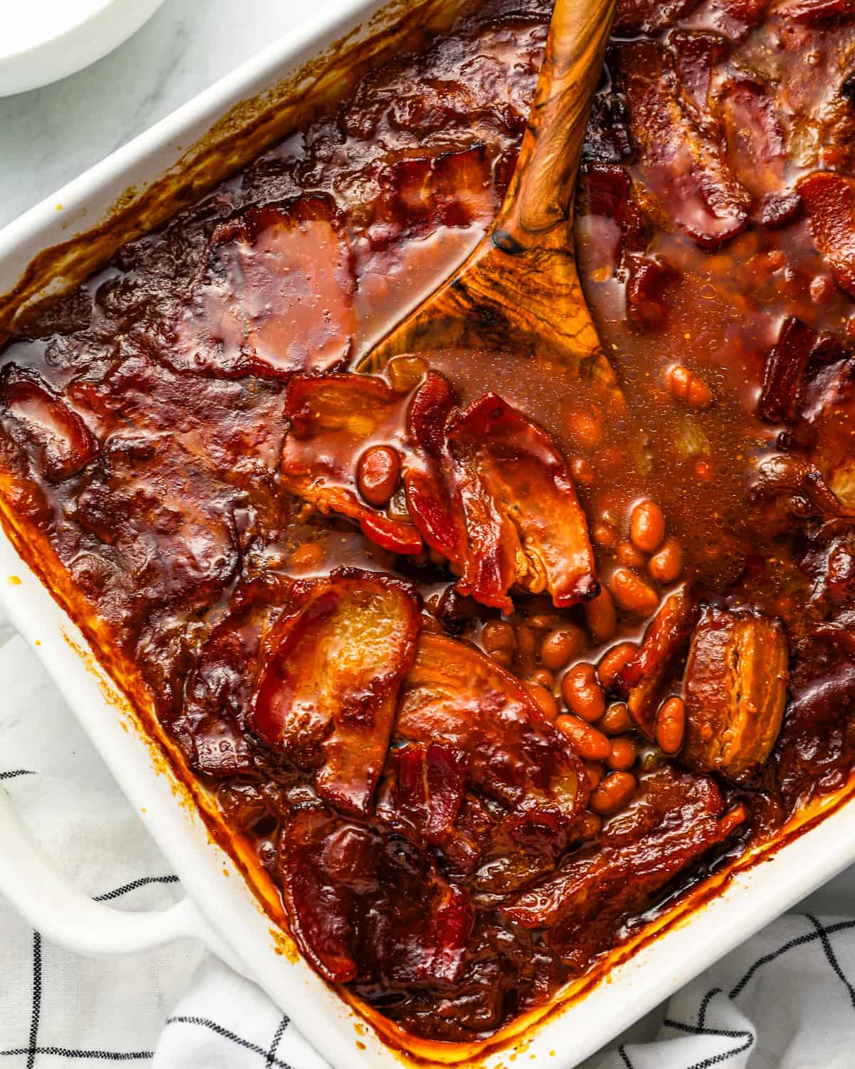 a large casserole dish filled with baked beans and slices of bacon.