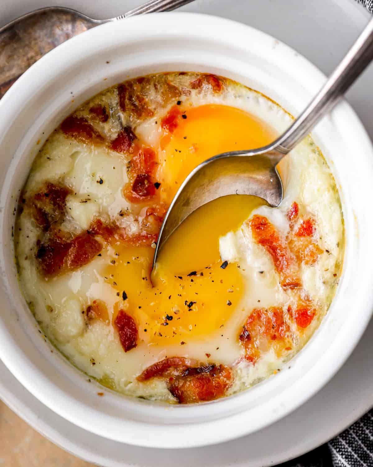 spoon digging into a cup of oven baked eggs, with bits of bacon and feta mixed in.