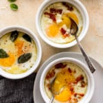 Three bowls of eggs with bacon and basil on a table.