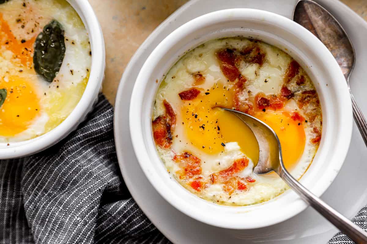 Two dishes of eggs with bacon and sage on a plate.