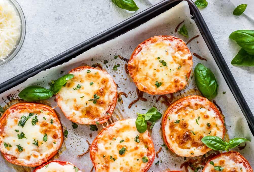 BAKED TOMATOES are a super quick and super easy side dish or appetizer for any occasion! These cheesy Baked Tomatoes with Mozzarella and Parmesan cheese are so simple yet incredibly delicious. They are always a hit when we make them and get eaten right away. These Baked Parmesan Tomatoes are just too tasty and fresh. angle shot of baked tomatoes with parmesan