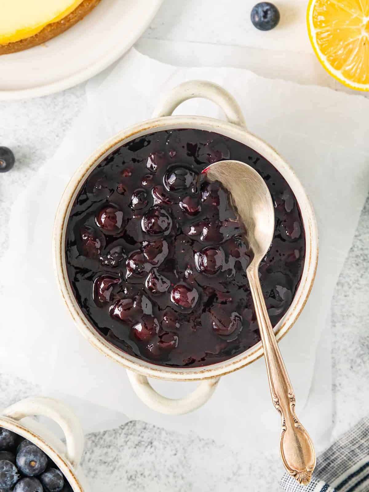 overhead view of blueberry compote in a small white cocotte with a spoon.