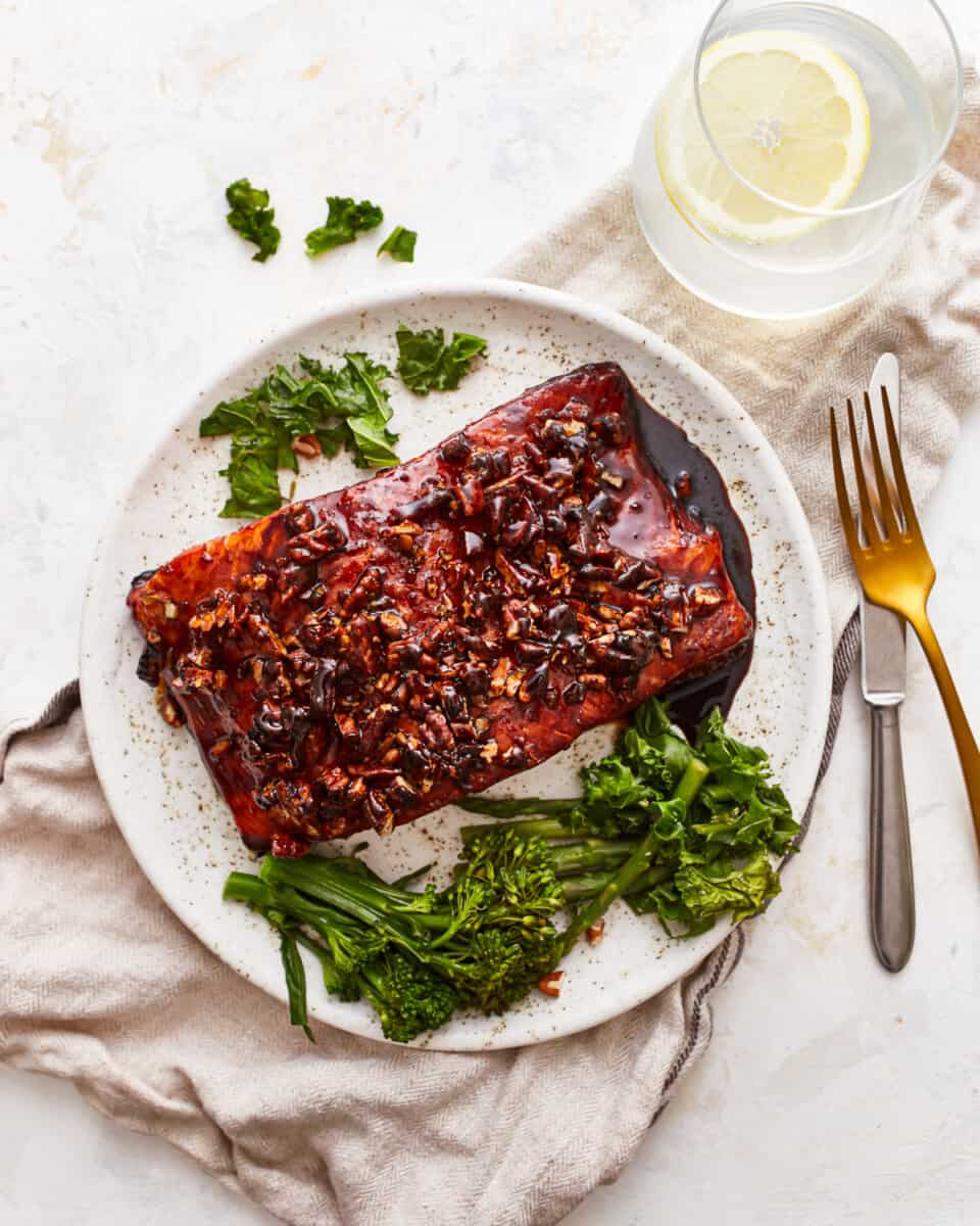 A plate with a piece of brown sugar salmon, broccoli and a glass of water.