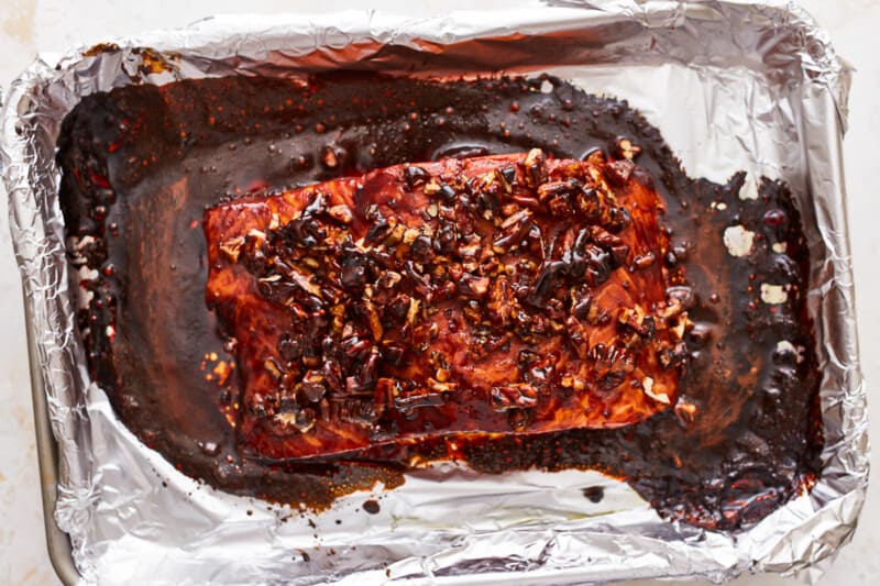 A piece of salmon on a sheet of foil topped with brown sugar glaze and pecans.