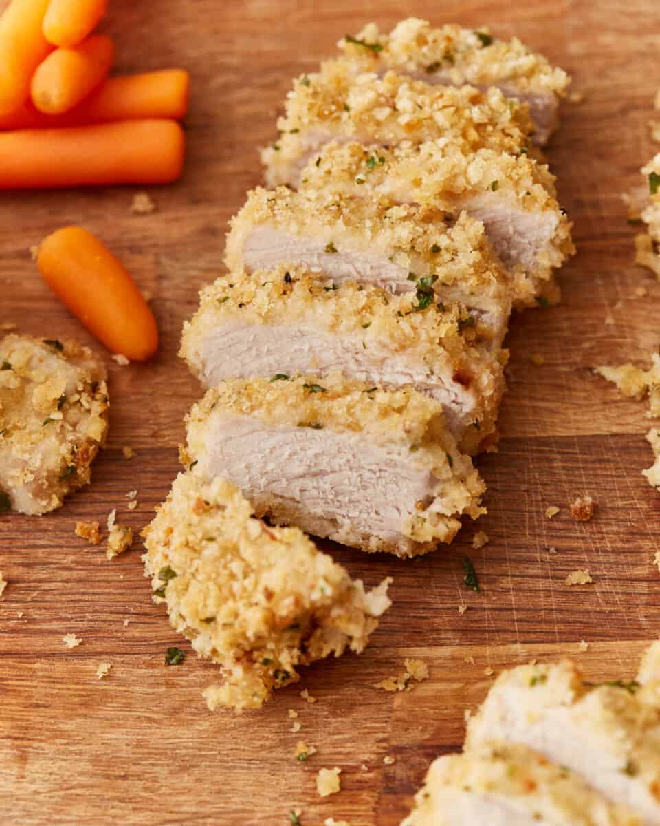a sliced baked pork chop with breading on a wooden cutting board with baby carrots.