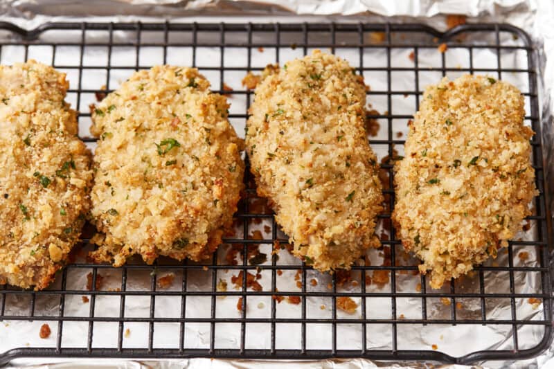 breaded pork chops on a cooling rack set in a baking sheet.