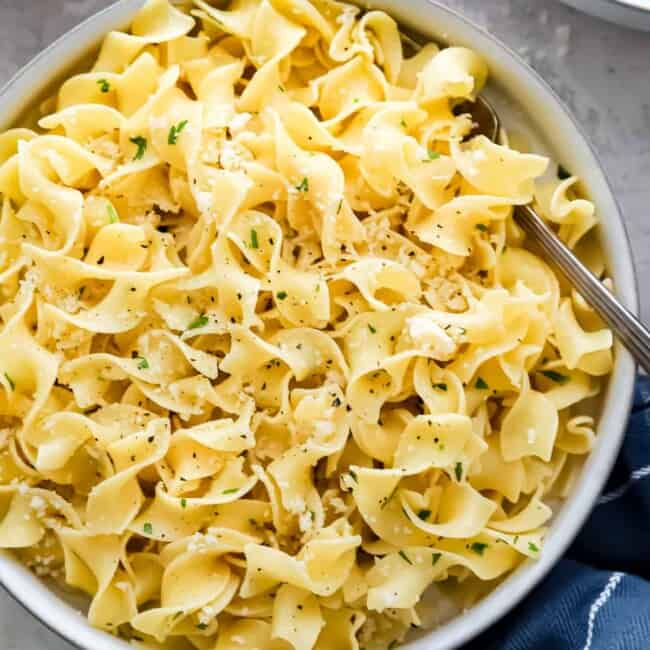Two bowls of pasta with parmesan cheese and parsley.