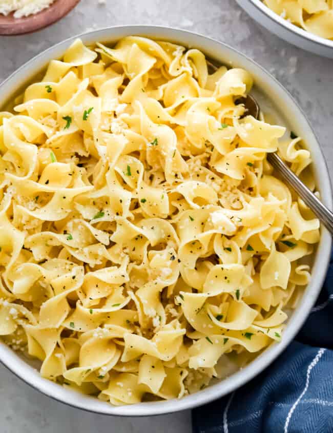 Two bowls of pasta with parmesan cheese and parsley.