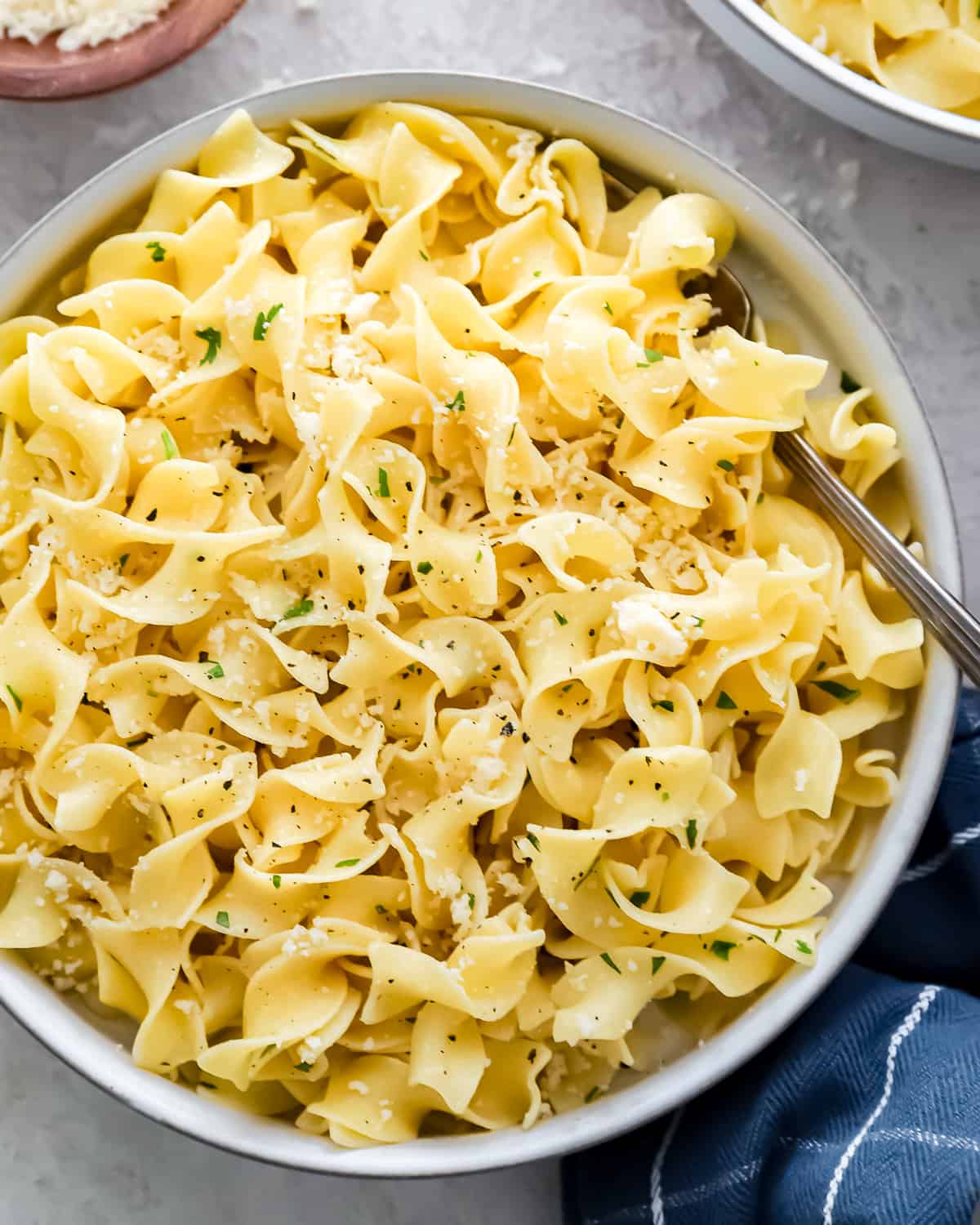close up on a bowl of egg noodles with butter, garlic, parsley, and cheese.