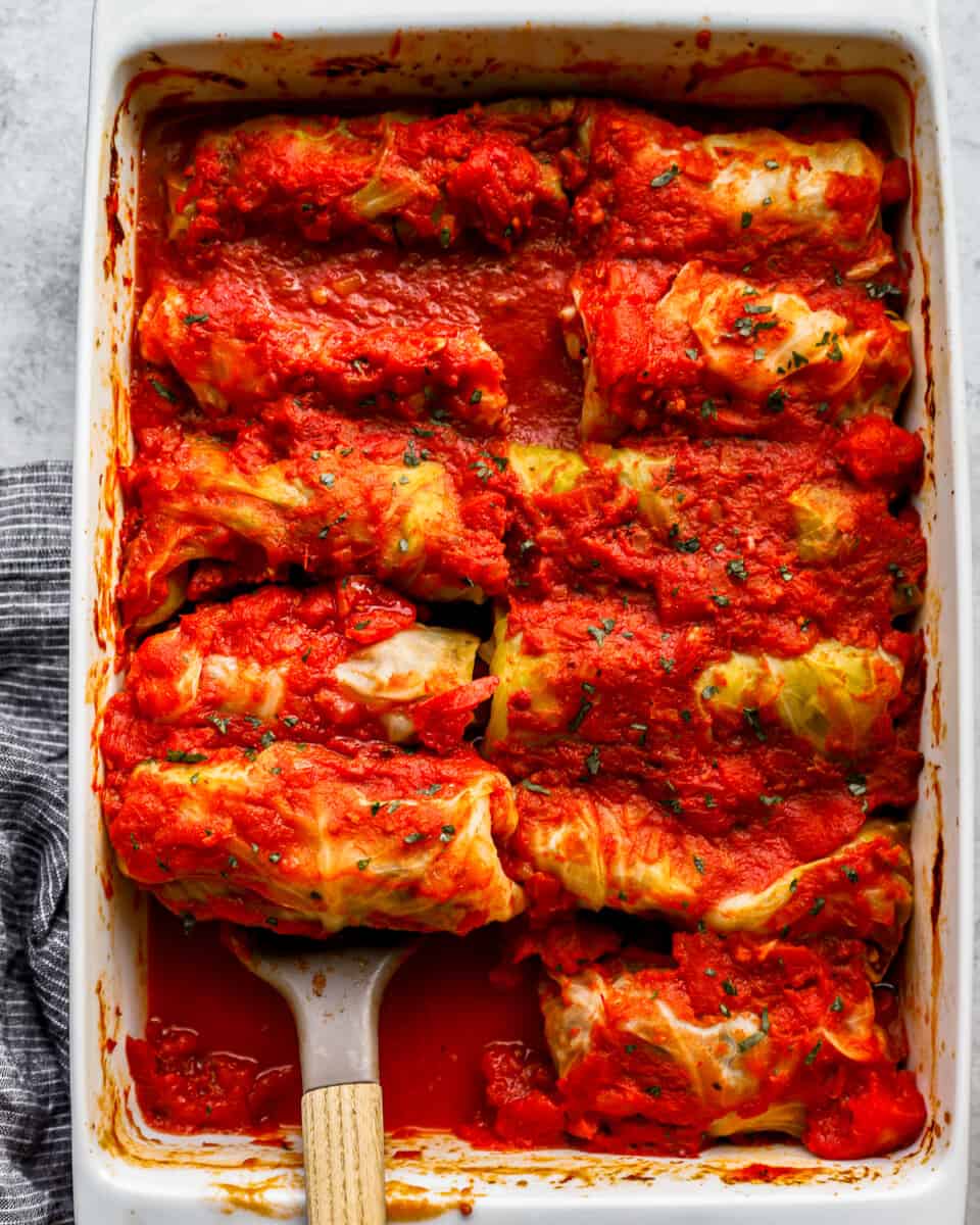 Stuffed cabbage rolls in a baking dish with a wooden spoon.