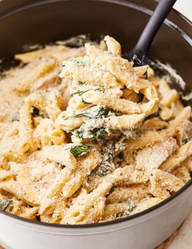 Penne pasta with chicken and spinach in a pan.