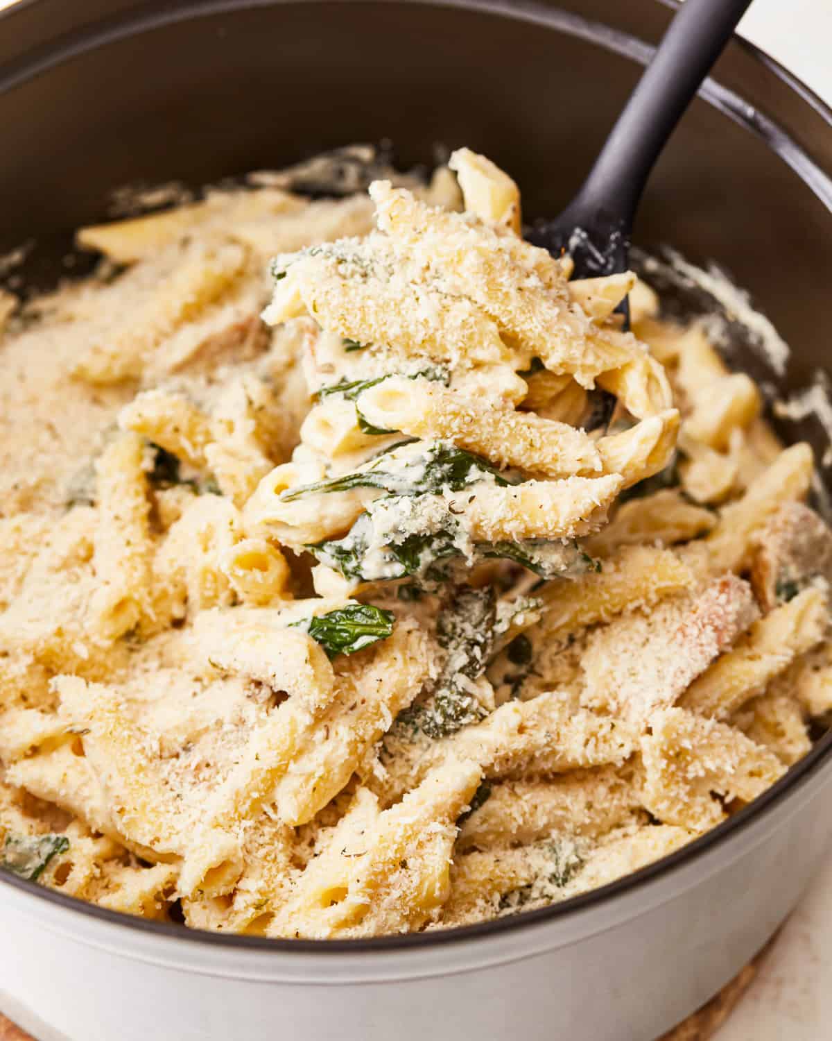 Penne pasta with chicken and spinach in a pan.