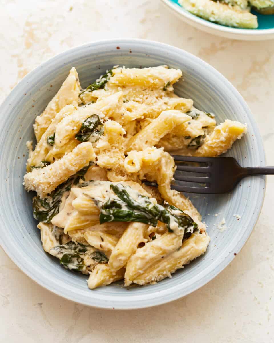 A bowl of pasta with spinach and chicken.