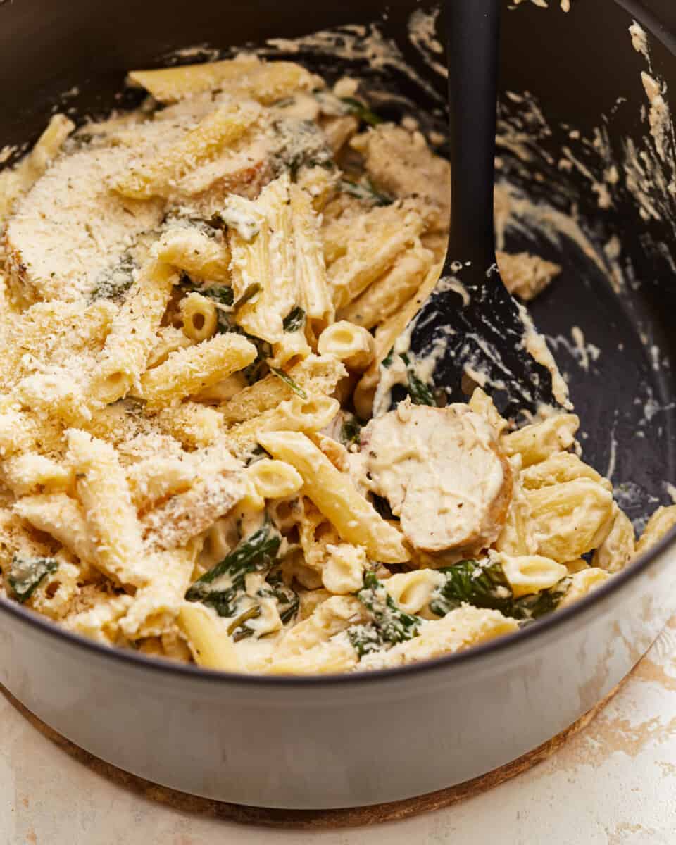 A pot of pasta with cheese and spinach in it.