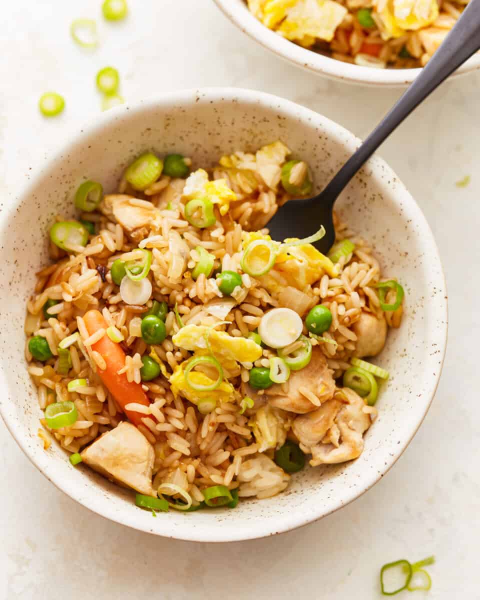 Two bowls of chicken fried rice with peas and carrots.