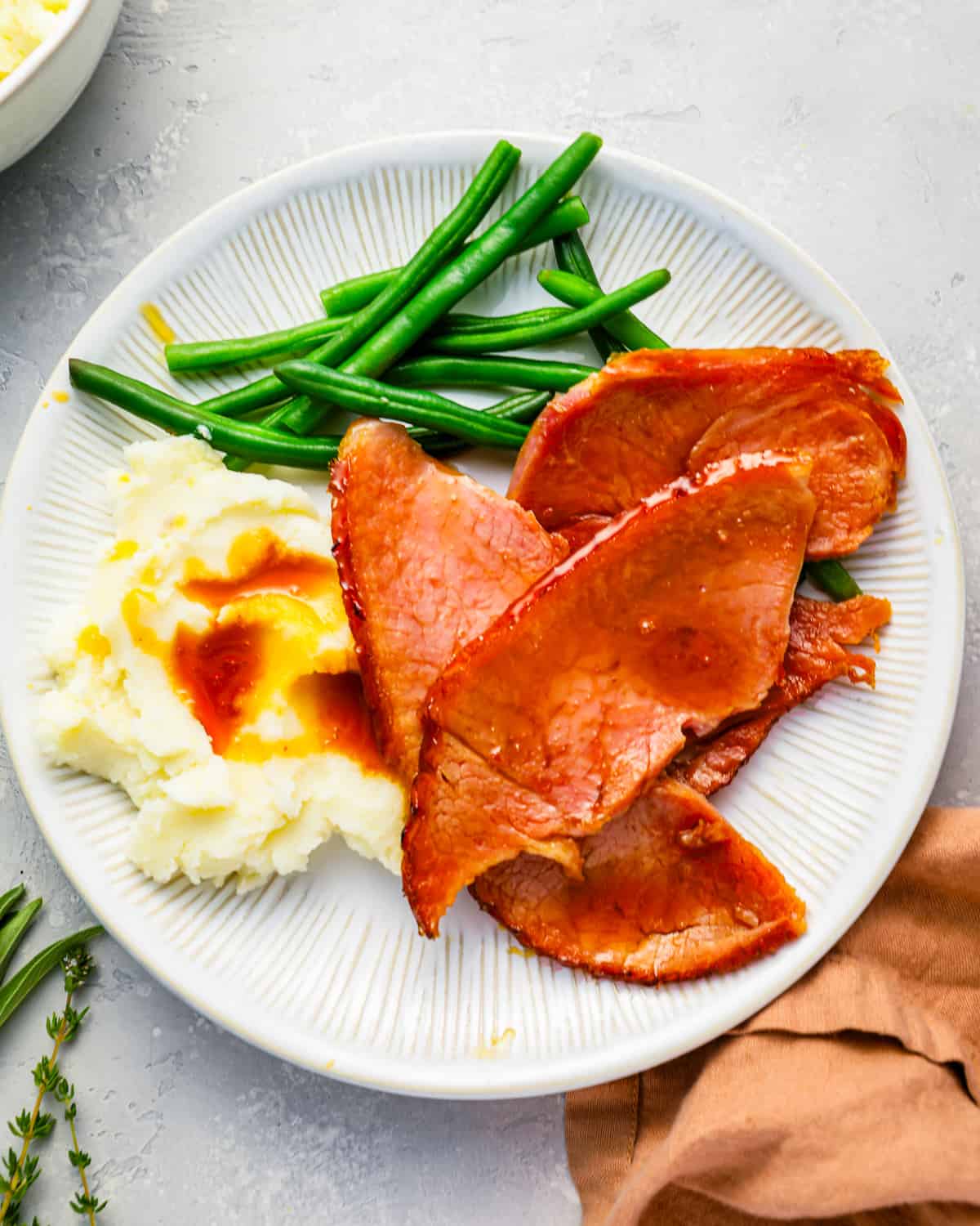 A plate with sliced of glazed ham, green beans and mashed potatoes.