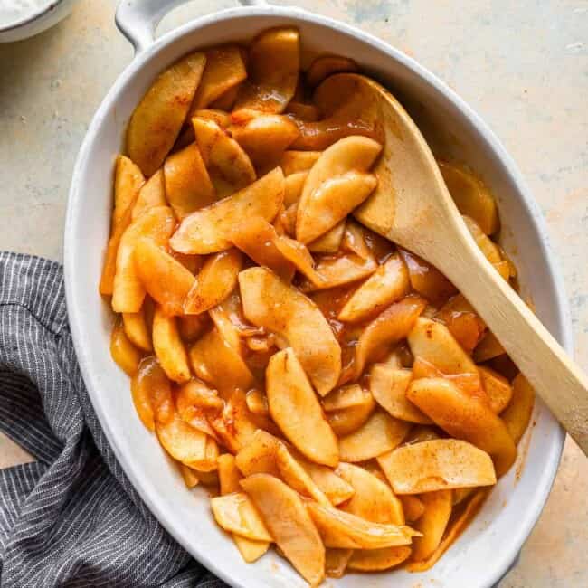 Apples in a dish with a wooden spoon.