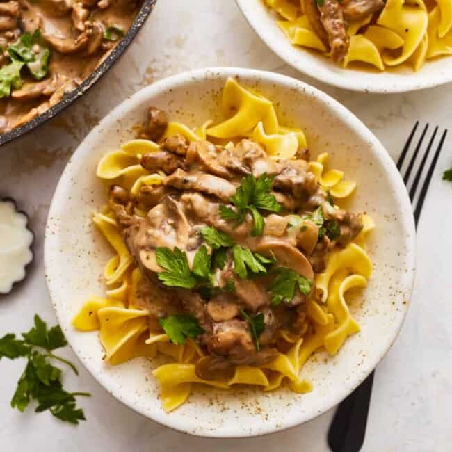 Two bowls of pasta with mushroom sauce and parsley.