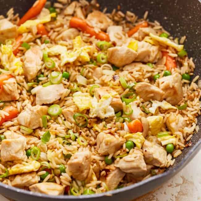 Chicken fried rice in a skillet with carrots and peas.