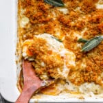 A casserole dish with a spoon and a sprig of sage.