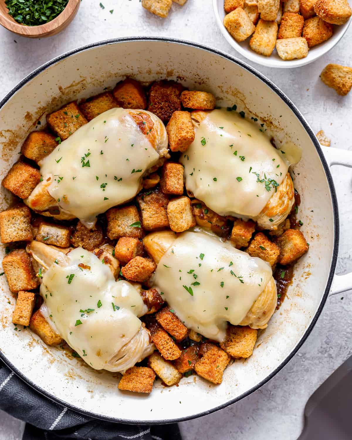 Chicken breasts in a skillet with croutons and cheese.