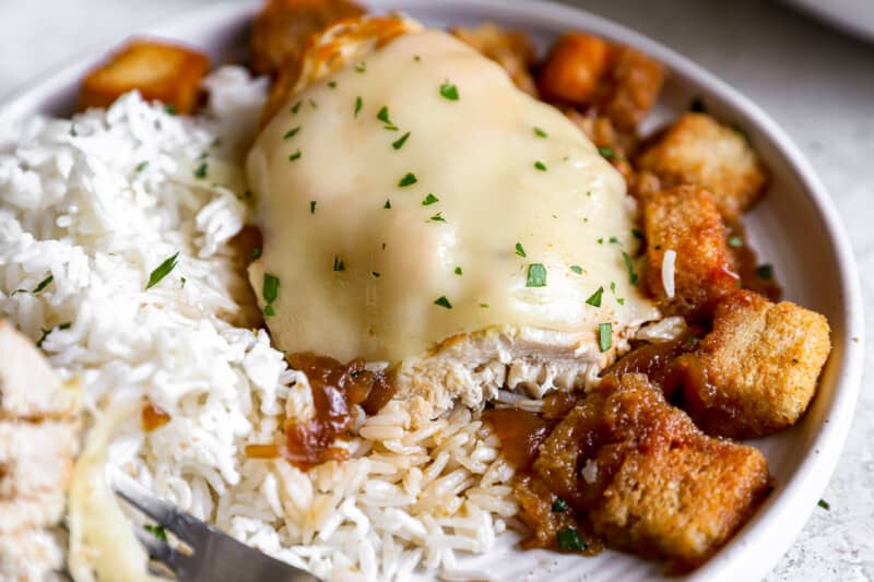 French onion chicken on a white plate with rice and croutons.