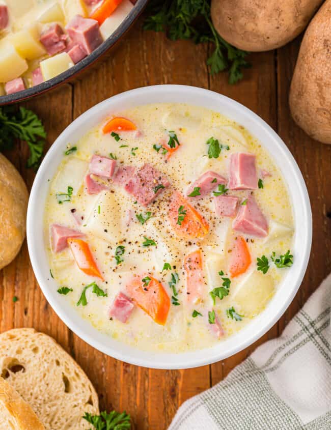 A bowl of soup with potatoes, carrots and ham.