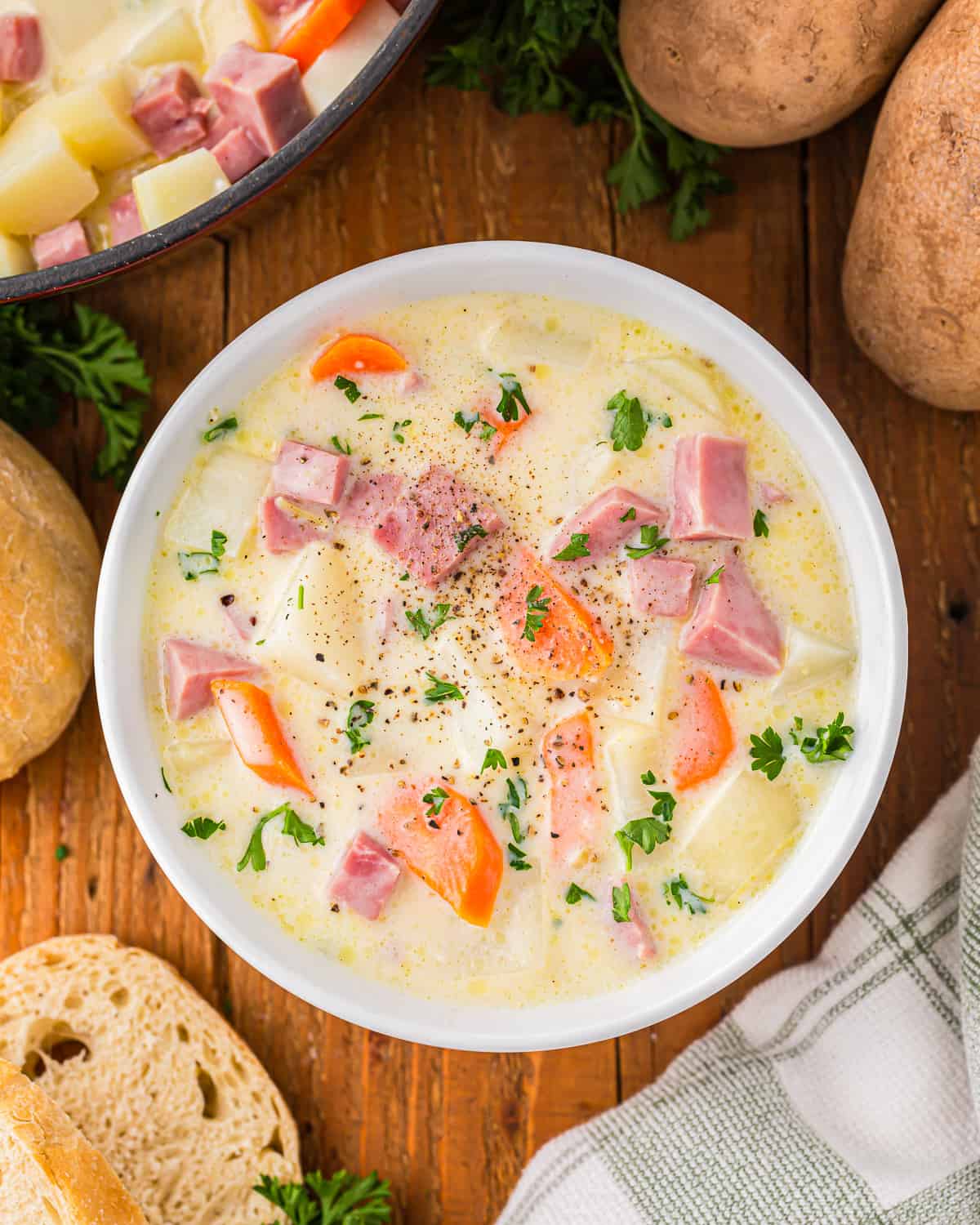 A bowl of soup with potatoes, carrots and ham.