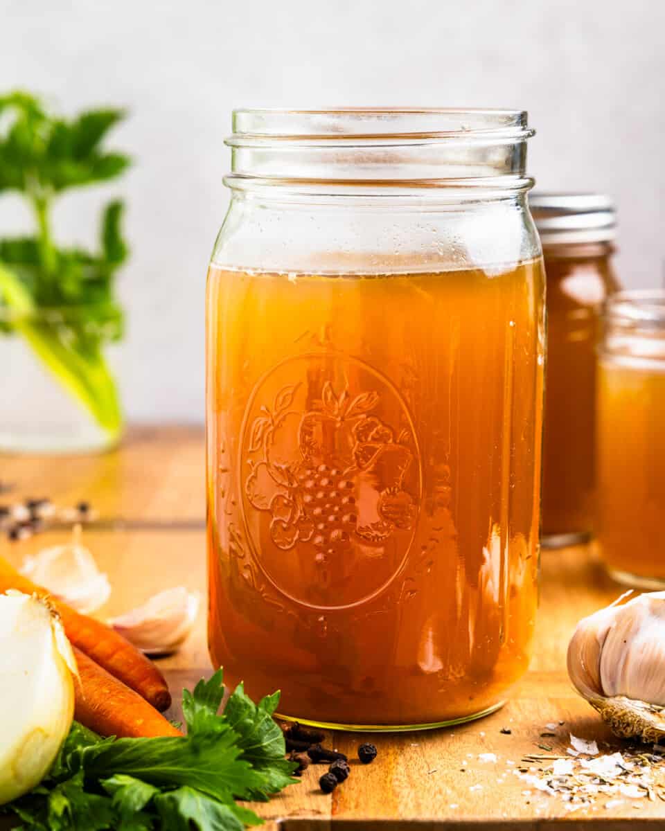 A mason jar with vegetables and herbs on a wooden table.