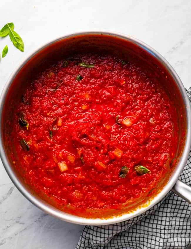 Tomato sauce in a pan with basil leaves.