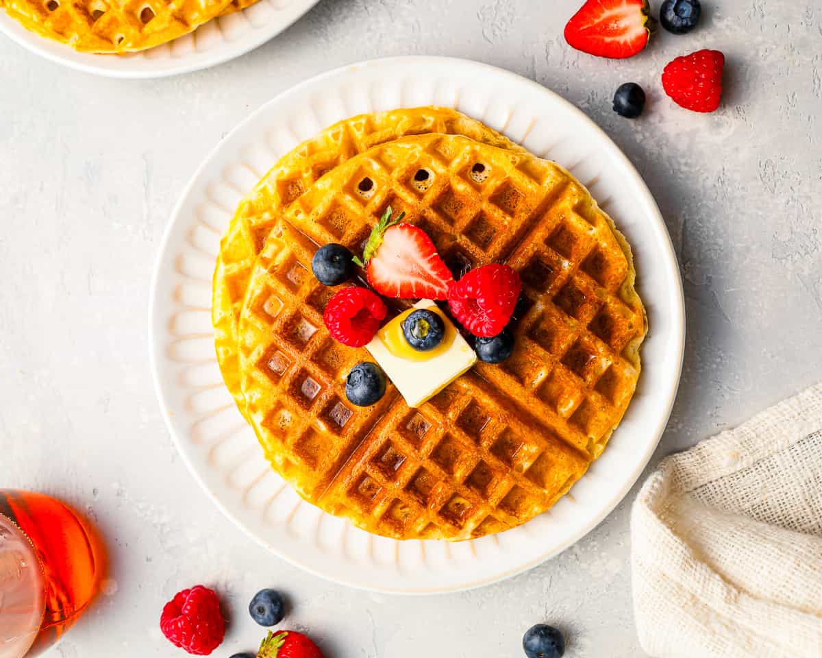 A plate of golden brown waffles with berries on them.