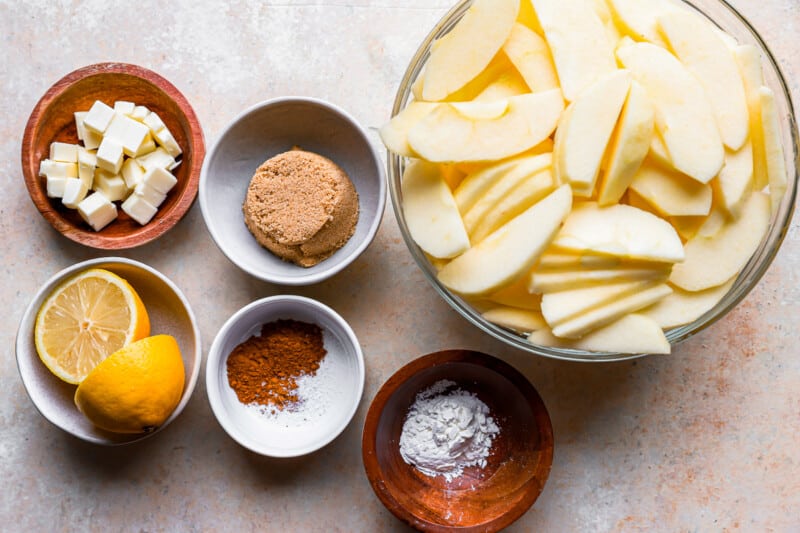 A bowl of apples, cinnamon, lemon, and other ingredients on a table.