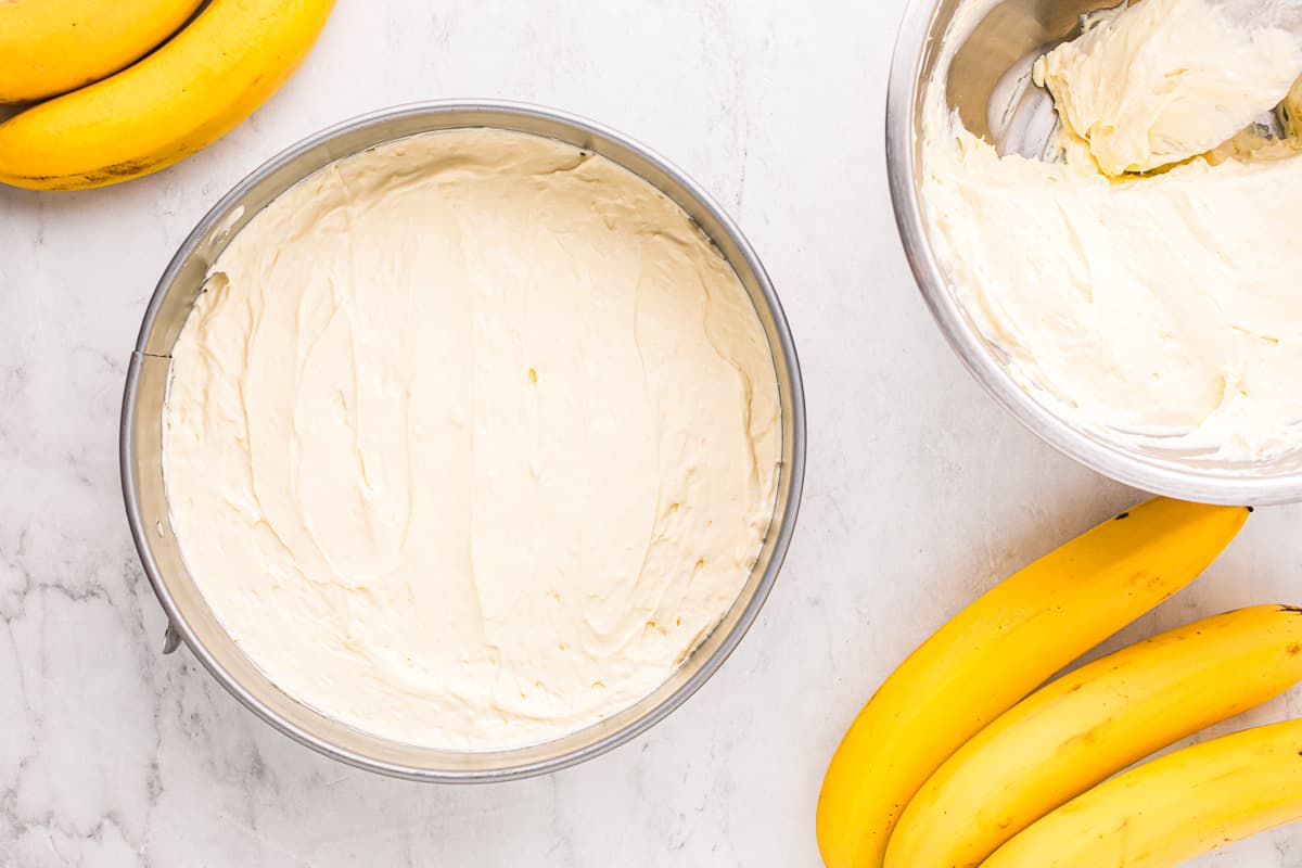 A bowl of icing next to a bowl of bananas.