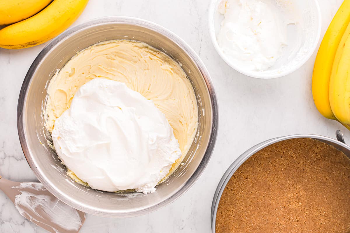 A bowl of whipped cream next to a bowl of bananas.