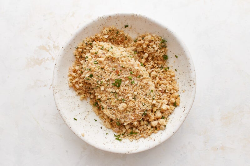 a pork chop coated in breadcrumbs in a white bowl.