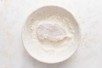 A white bowl with flour in it on a white background.