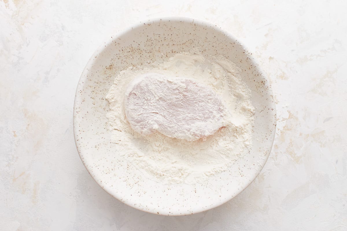 A pork chop in flour in a bowl. 