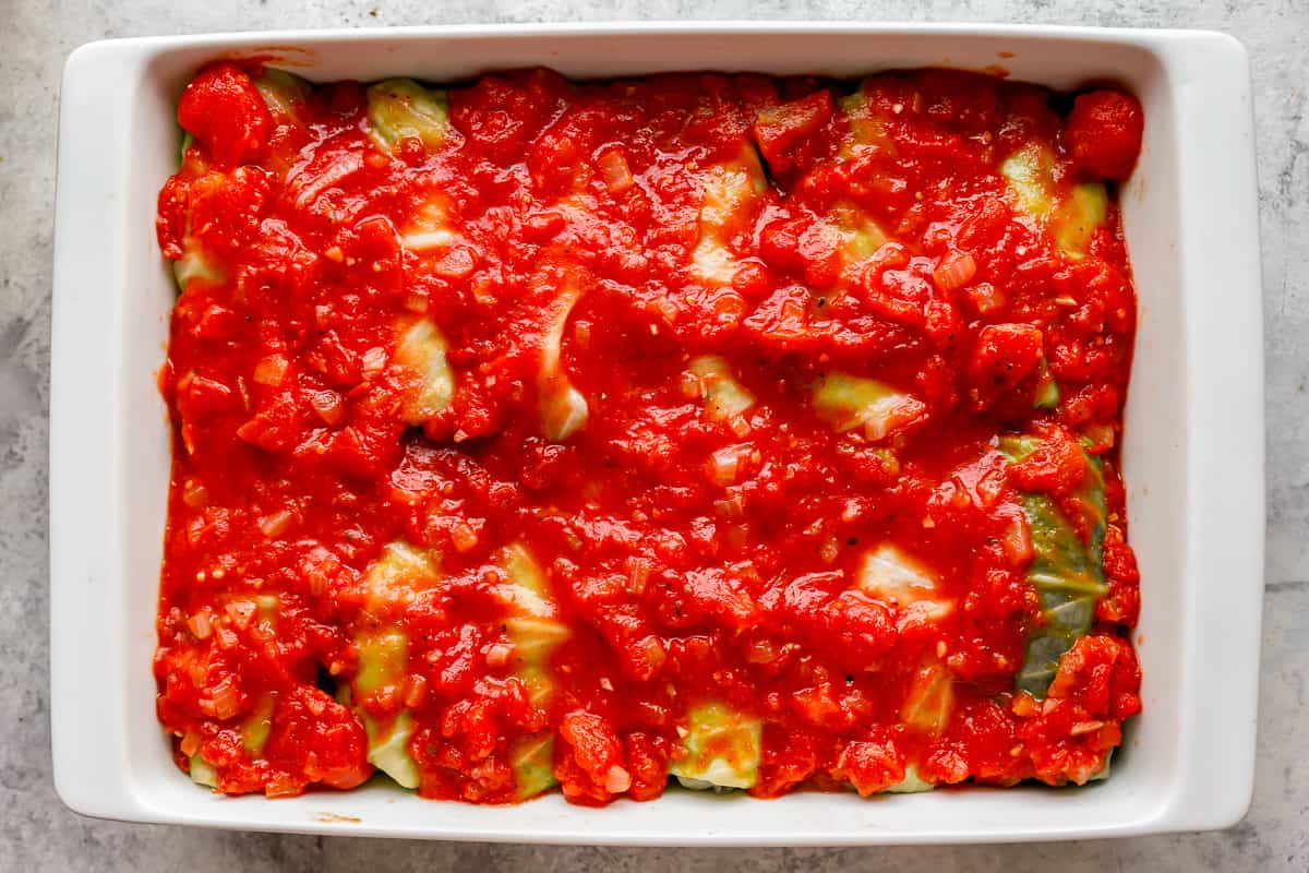 A dish filled with stuffed zucchini rolls with tomato sauce.