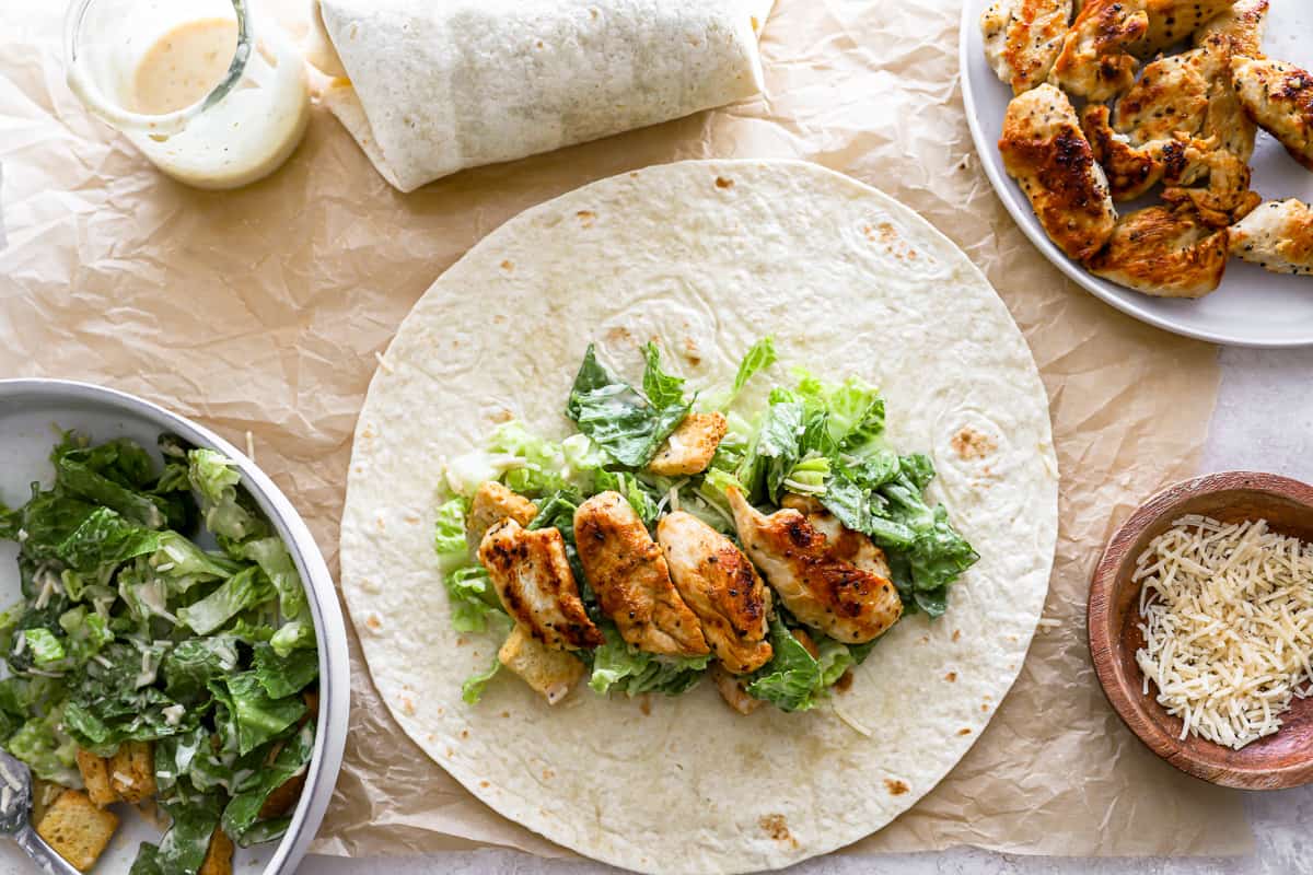 Salad and pieces of chicken lined up at the center of a tortilla.