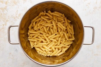 Penne pasta in a metal pot on a white surface.