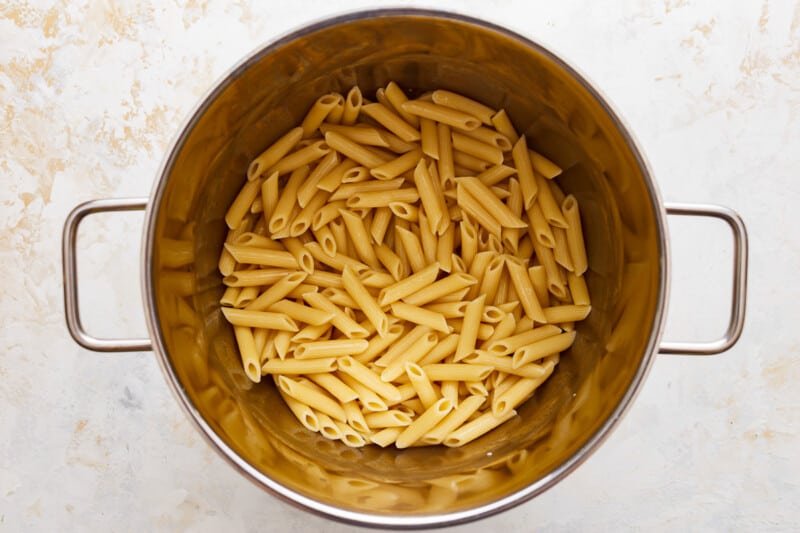 Penne pasta in a metal pot on a white surface.