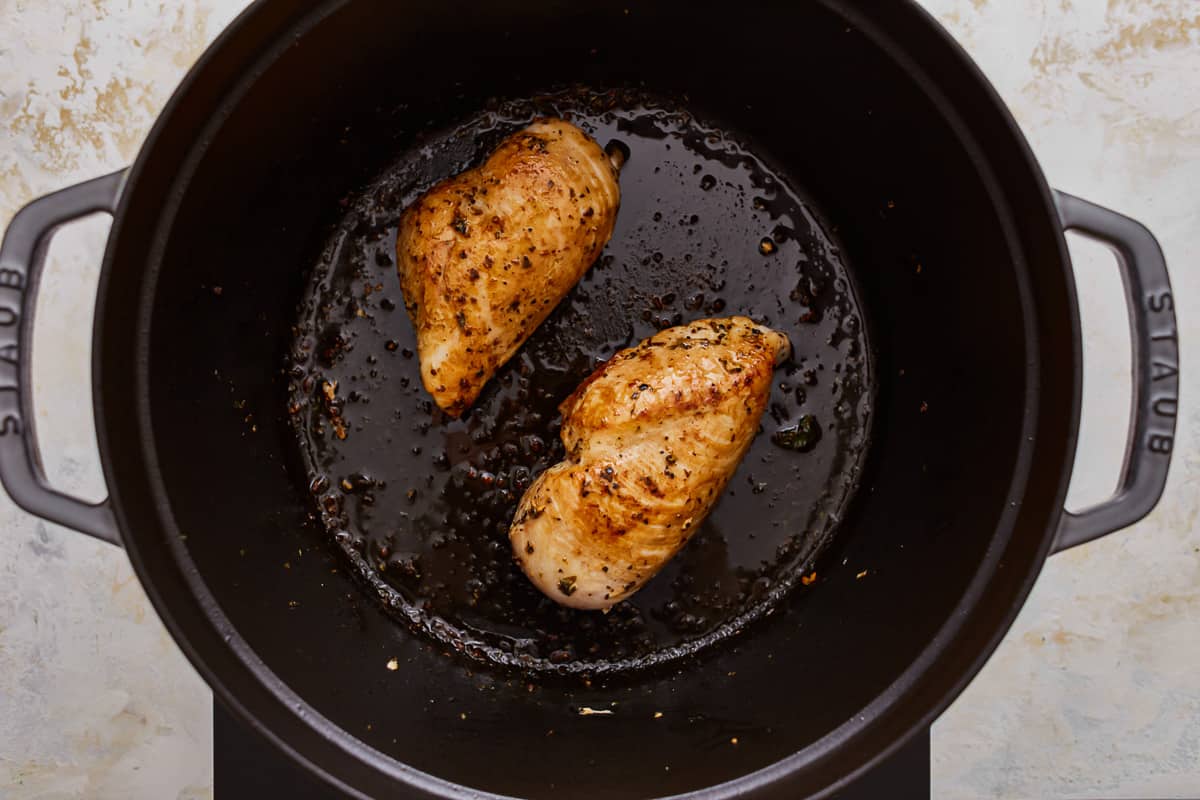 Two chicken breasts are being cooked in a skillet.