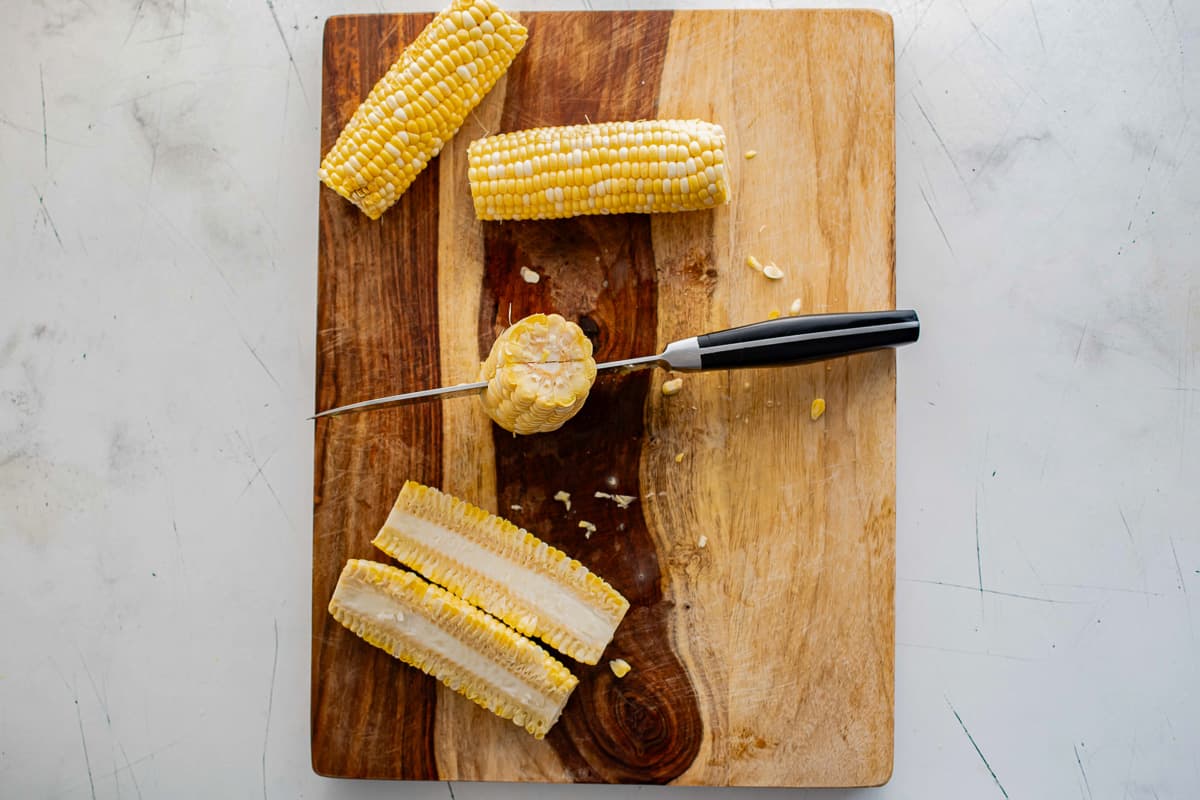 corn on the cob being cut into riblets on a cutting board.