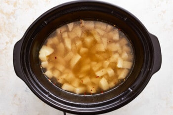 A crock pot filled with a mixture of apples and spices.